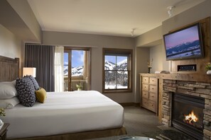 A hotel room with a large bed, a fireplace, a television, and a view of snow-covered mountains.