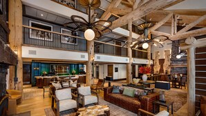 Un interior espacioso, de varios niveles, con vigas de madera, una zona de estar central con sofás y sillones, y un área de bar/lounge.