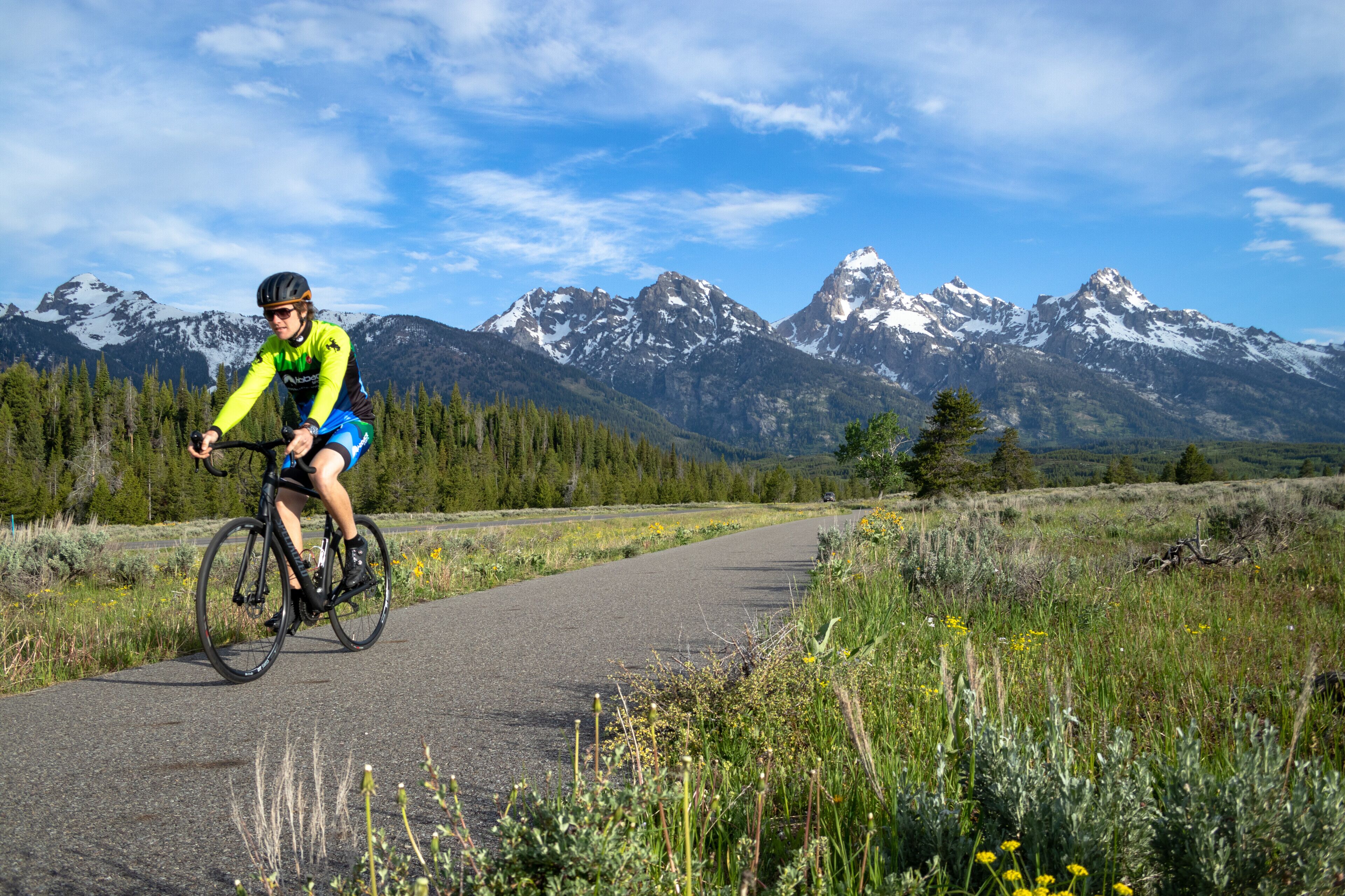 A cyclist on a paved path with a mountainous backdrop.