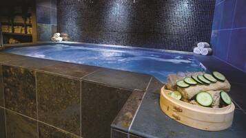 Uma área de spa com hidromassagem, paredes revestidas e uma banheira de madeira com fatias de pepino.