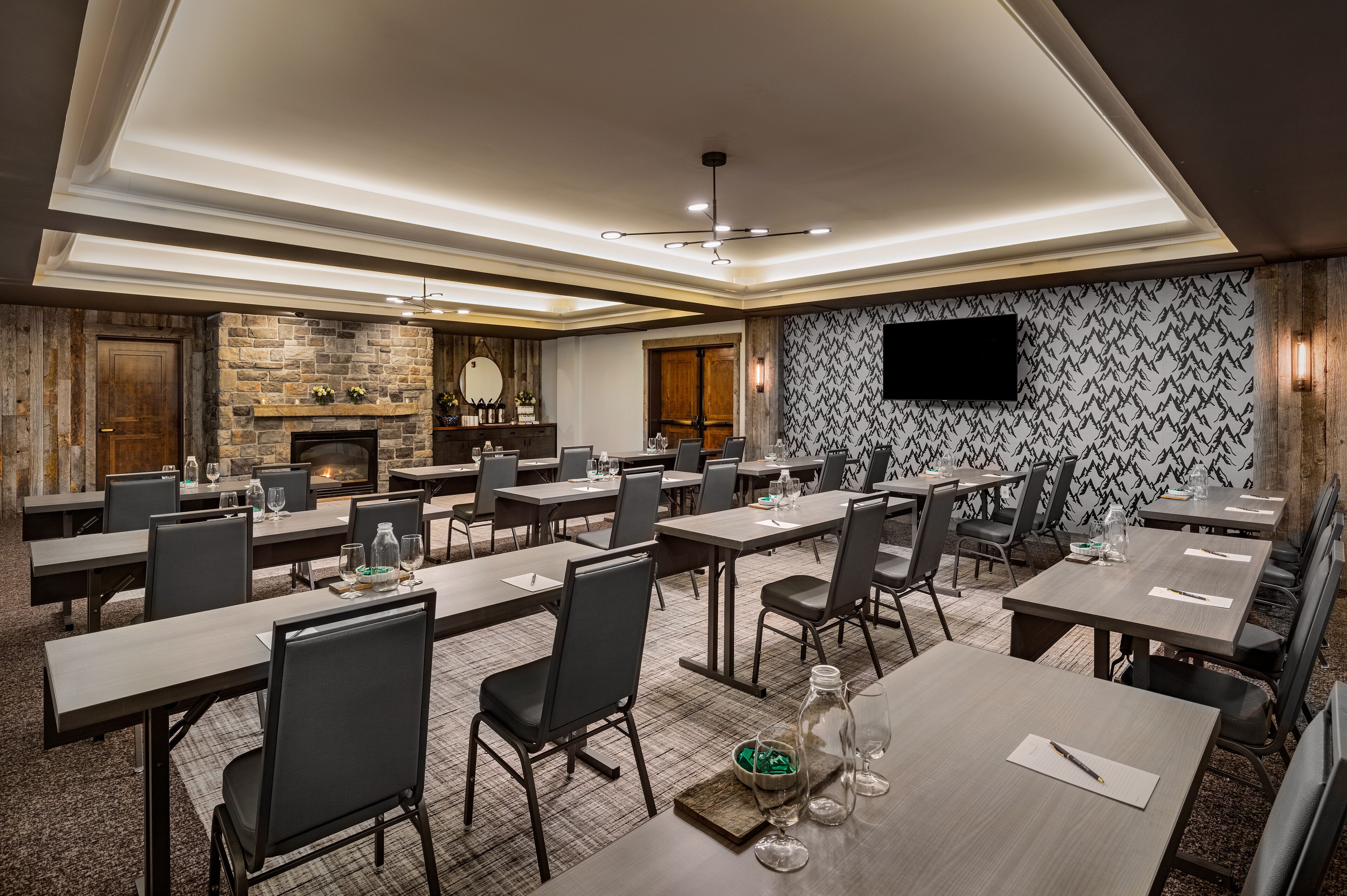 A conference room with multiple tables and chairs, a fireplace, and a flat-screen TV on the wall.