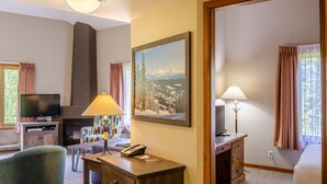 Habitación de hotel con televisión, escritorio con lámpara, pintura de un paisaje nevado y chimenea.