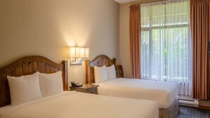 Habitación de hotel con dos camas, una mesita de noche con lámpara, una ventana con cortinas y un termostato.