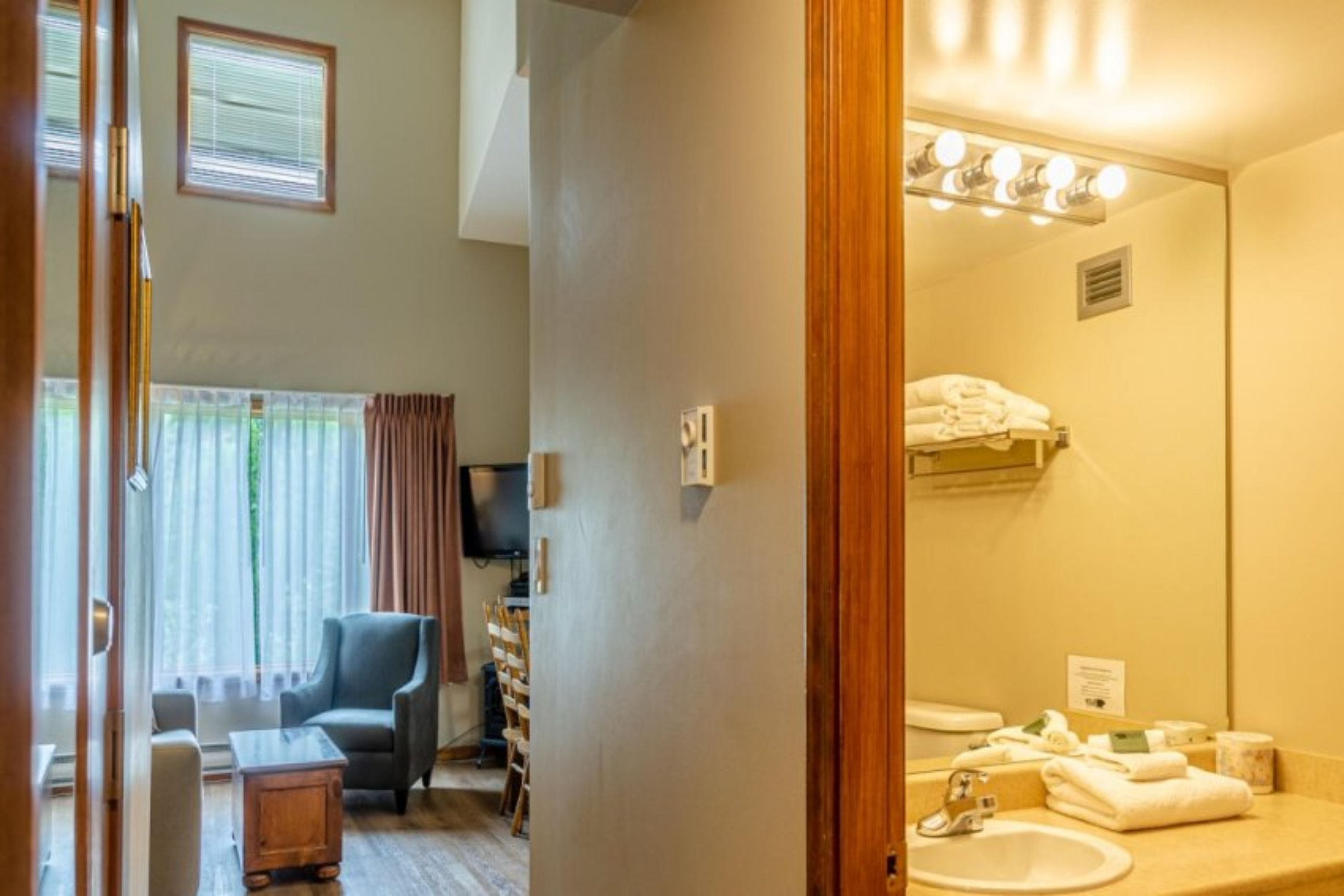 A hotel room with a sitting area, a large mirror, a sink, and a television.