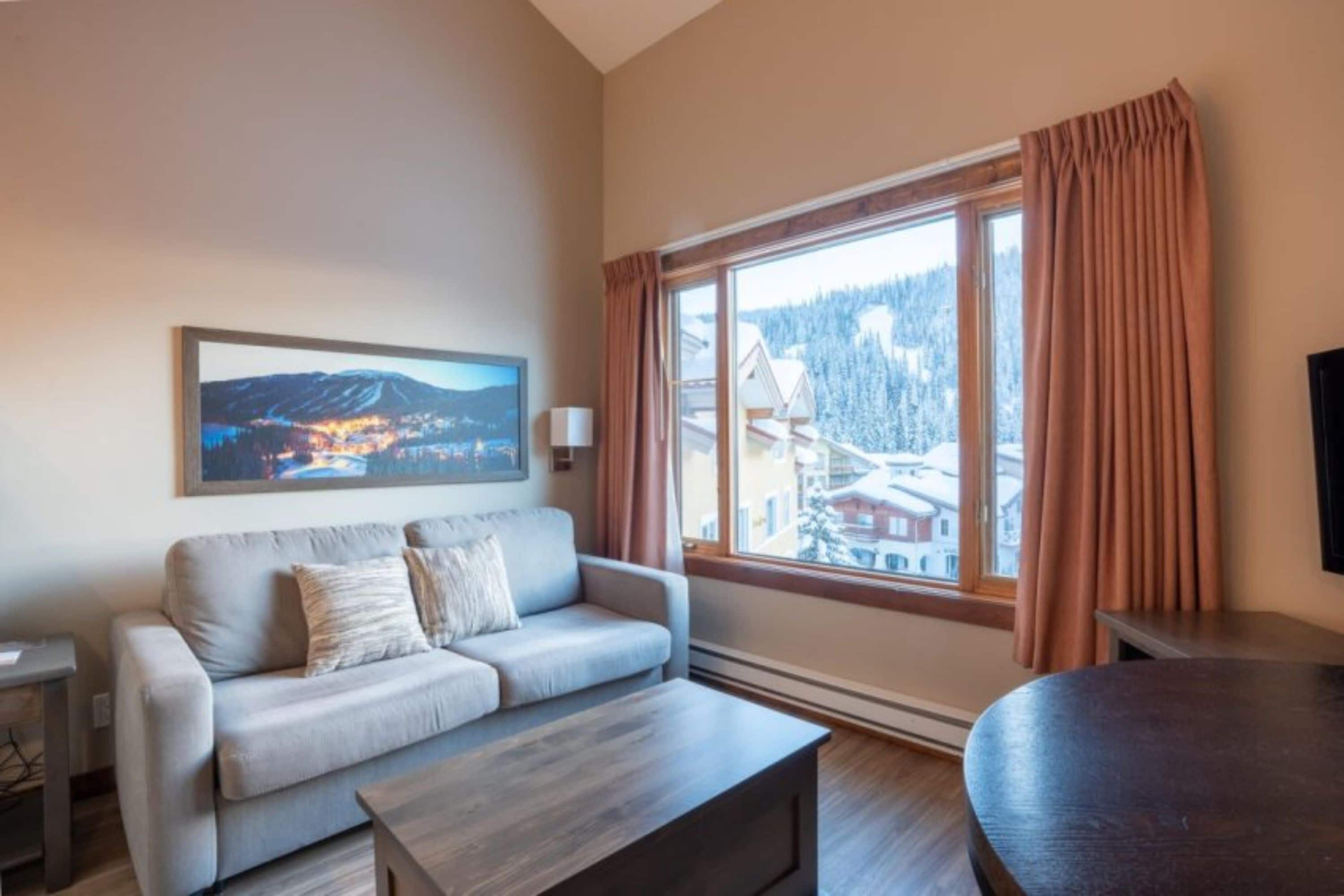 A modern living room with a sofa, a coffee table, and a large window with curtains.