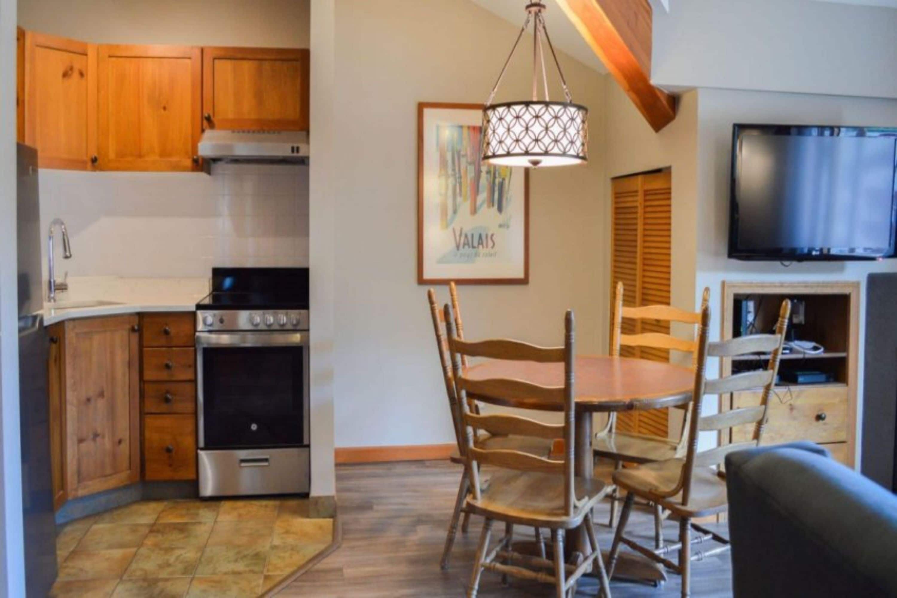 A compact kitchen with wooden cabinets, a stove, and a dining area with a table and chairs.