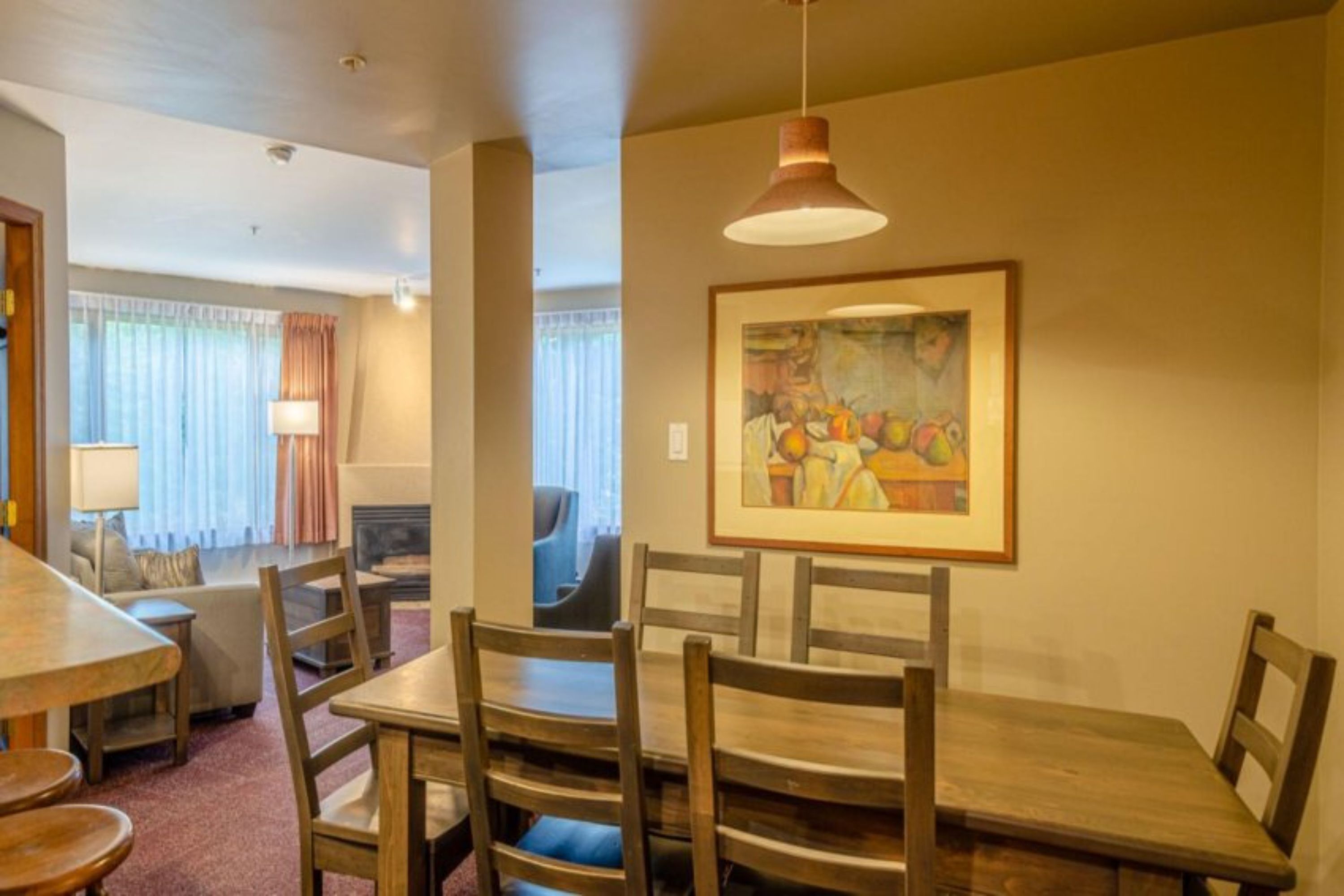 A dining area with a wooden table and chairs, a painting on the wall, and a lamp.