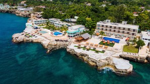 Vista aérea de un hotel costero con piscina, tumbonas y vistas al mar.