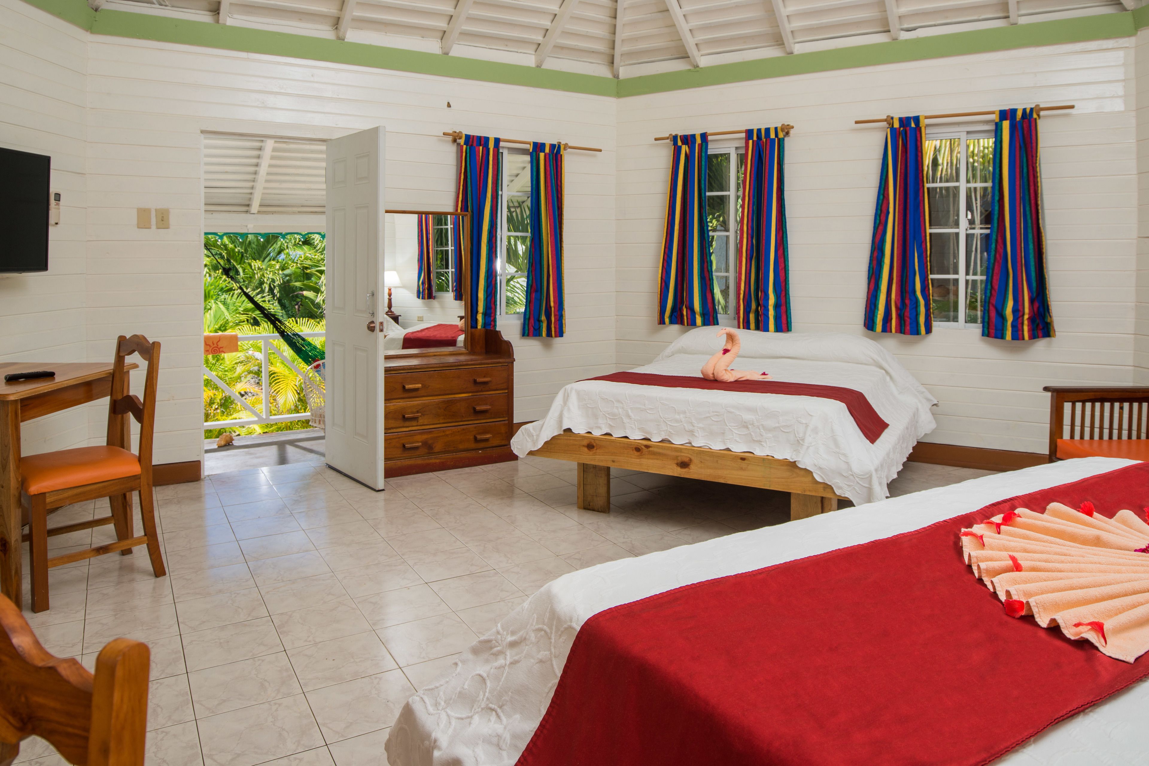 A hotel room with a bed, a desk, and a chair. There is a balcony with a view of greenery.