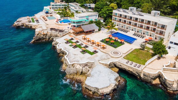 Un complejo turístico frente al mar, con piscina, zonas de descanso y vistas al océano.