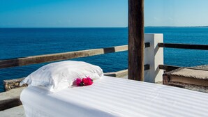 Una cama con ropa blanca y una flor rosa, con vistas a un mar azul cristalino.