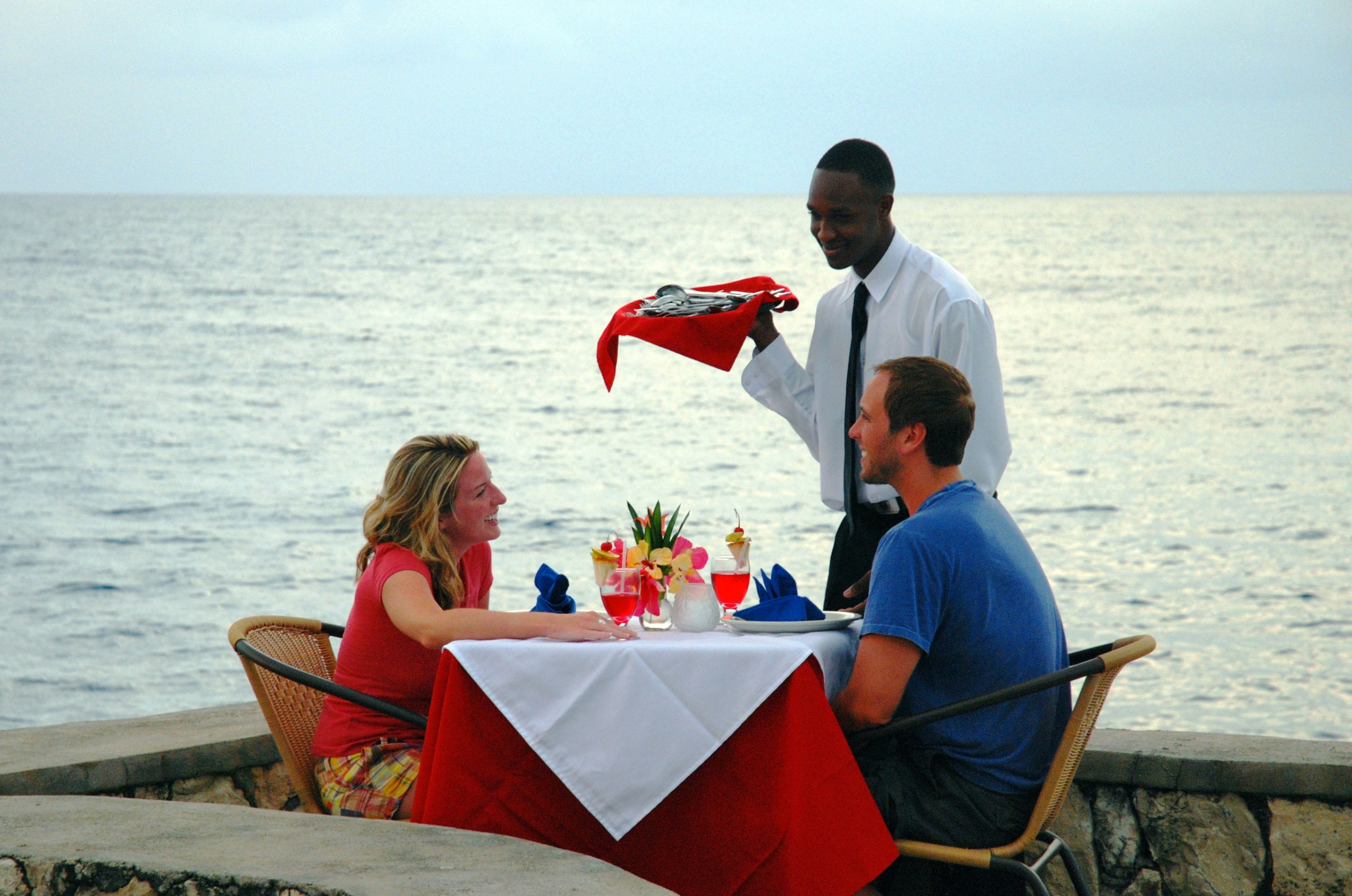 Mesa servida con bebidas y un mantel rojo, con vistas al mar.
