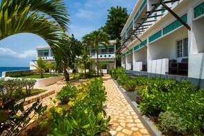A hotel with a stone pathway, lush greenery, and a view of the sea.