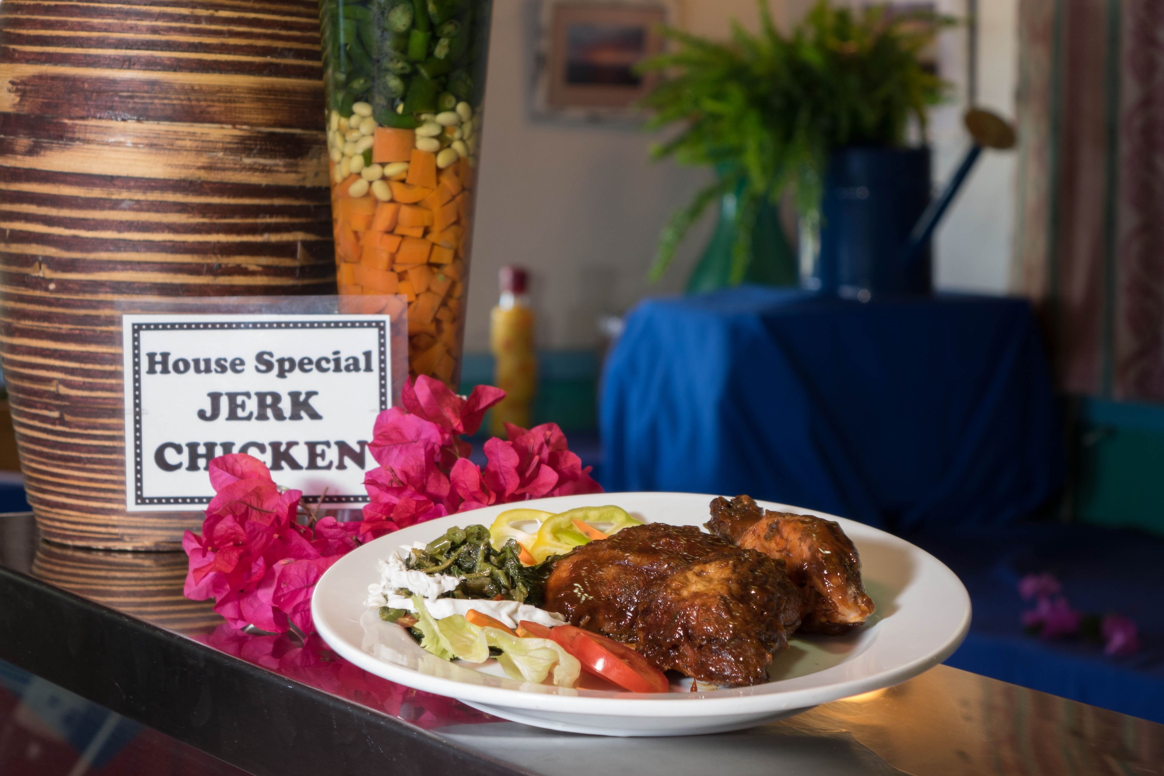 Ein Teller Jerk Chicken mit Gemüse und einem Schild, das es als Hausspezialität kennzeichnet.