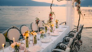 Una mesa dispuesta para una comida, con velas, jarrones con flores y vistas al agua.
