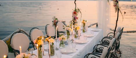 A table set for a meal with candles, vases with flowers, and a view of the water.
