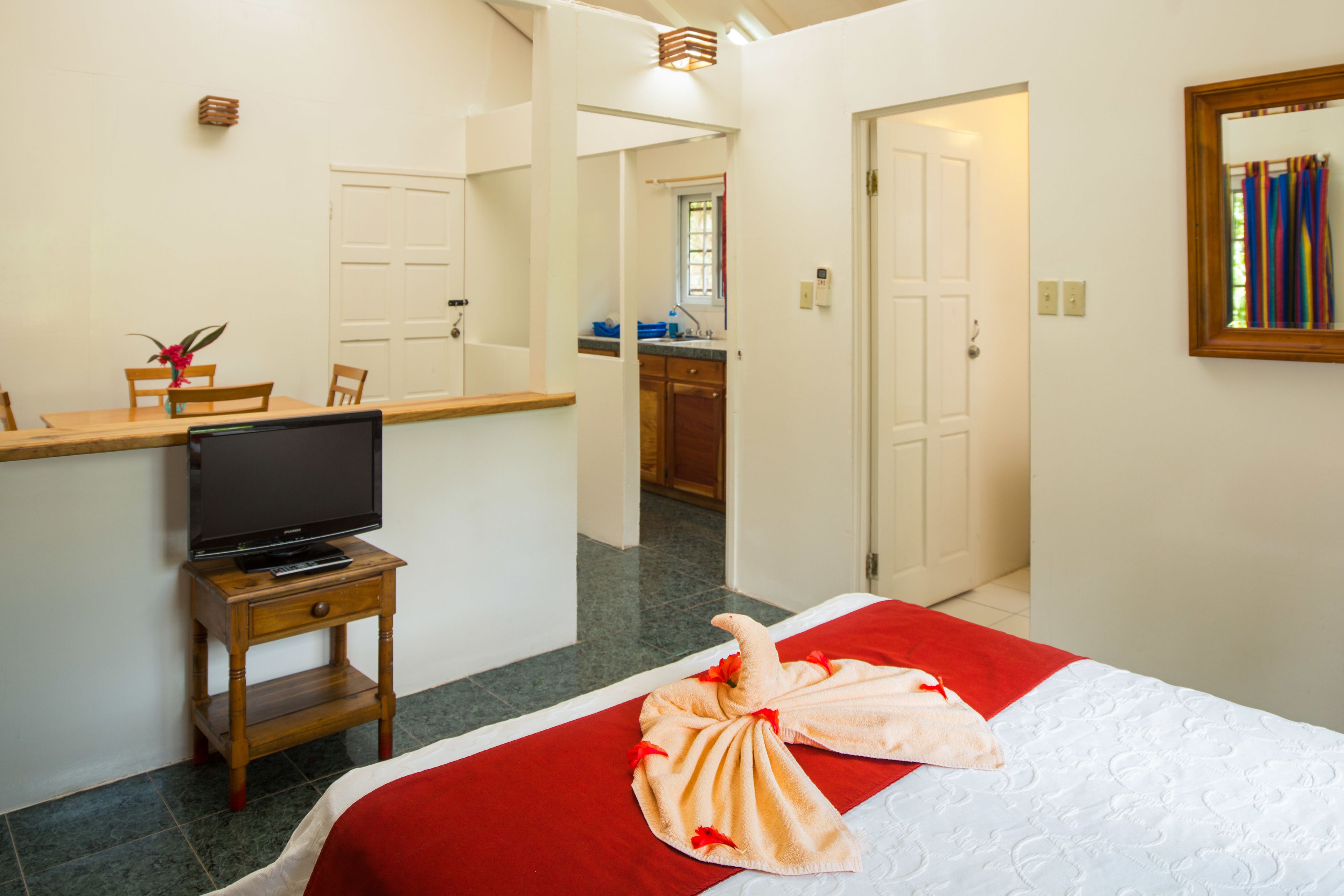 A hotel room with a bed, a TV on a wooden side table, a bathroom visible through an open door, and a mirror on the wall.