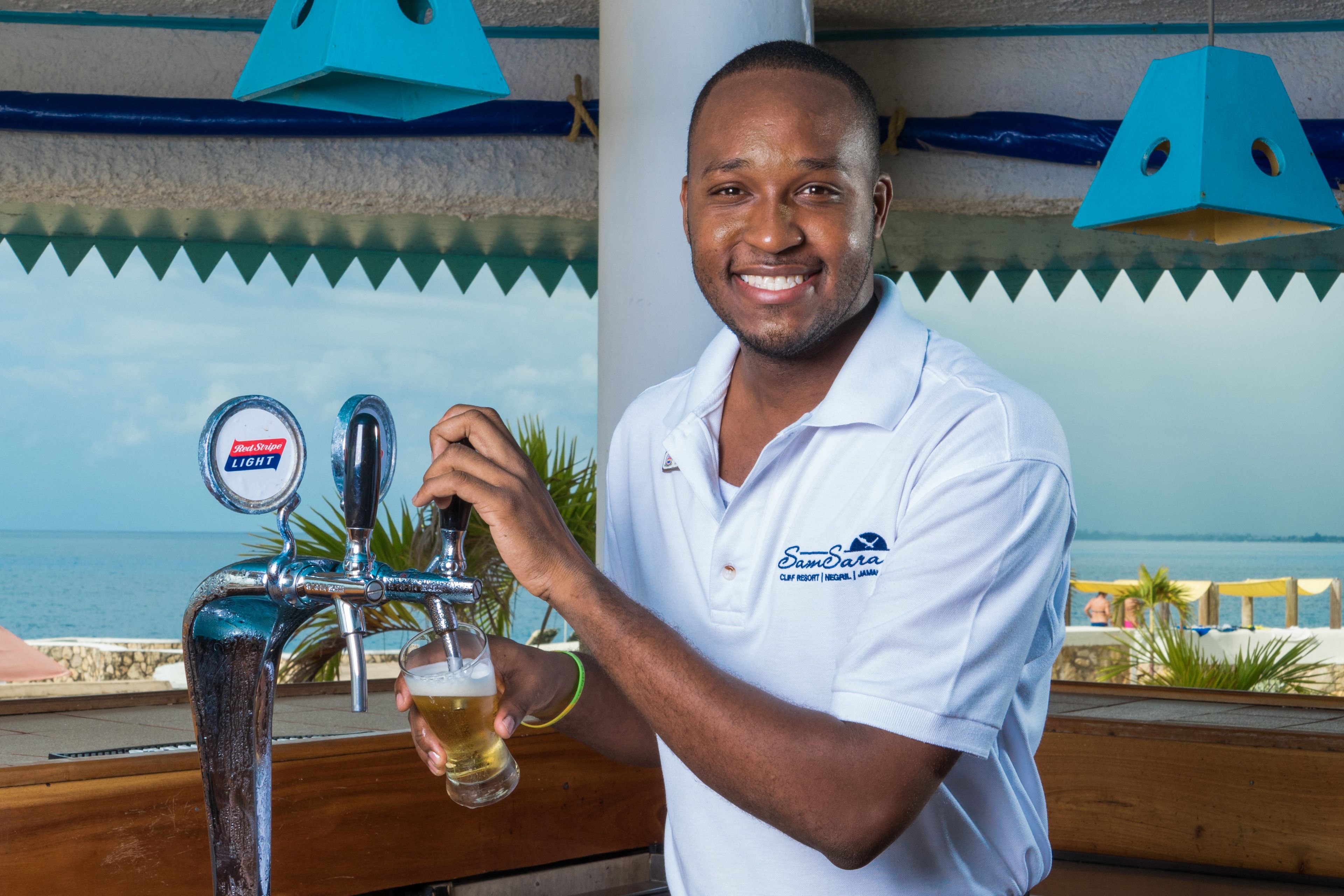 A person pouring beer from a tap with a view of the ocean in the background.