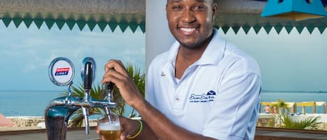 A person pouring beer from a tap with a view of the ocean in the background.