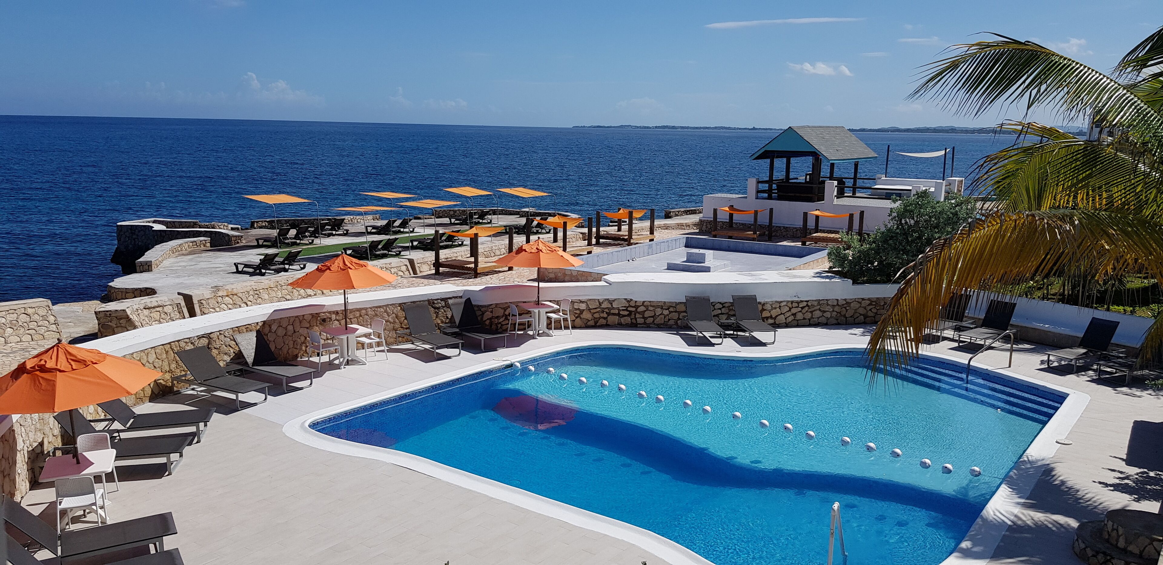 Un espace piscine avec des chaises longues et des parasols, un belvédère et une vue sur la mer.
