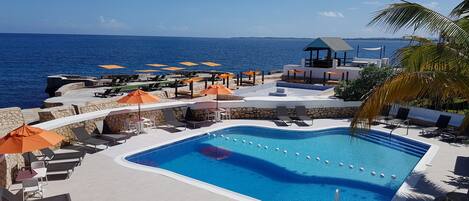Un espace piscine avec des chaises longues et des parasols, un belvédère et une vue sur la mer.