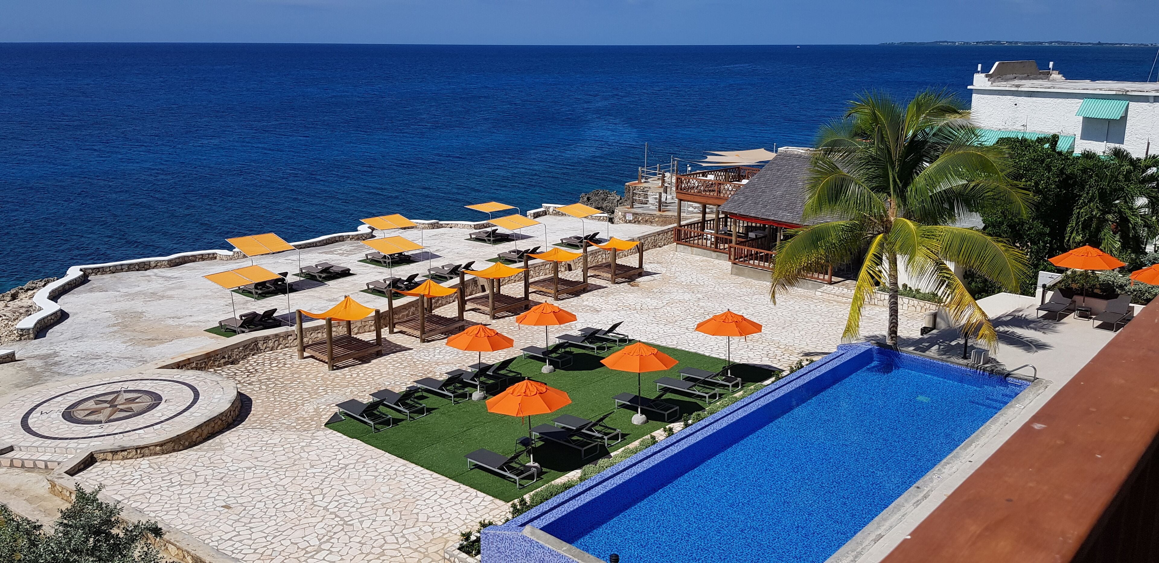 A poolside area with lounge chairs and umbrellas, a pool, and a view of the ocean.