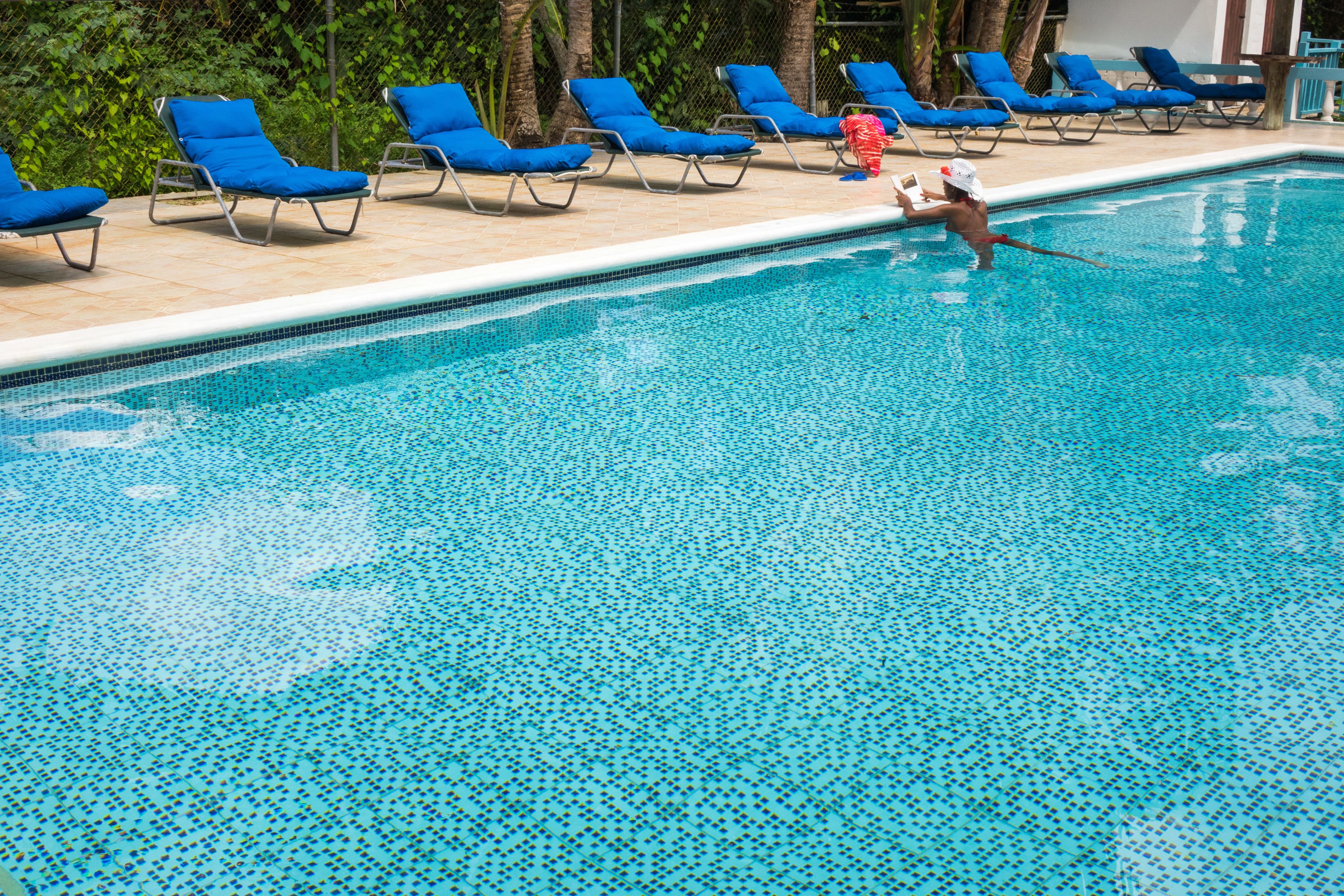 A swimming pool with blue lounge chairs and a person in the water.