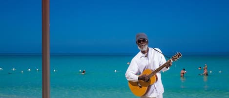 A man playing guitar under a beach umbrella.
