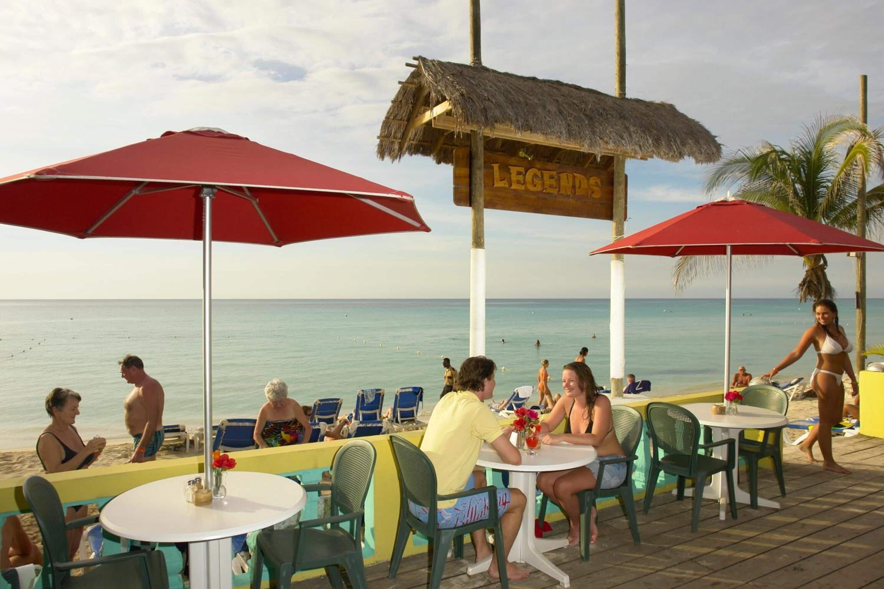 A beachside restaurant with outdoor seating, a thatched roof structure labeled "LEGENDS", and a view of the ocean.
