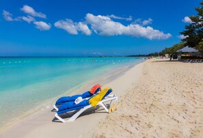 A beach with clear turquoise water, a sandy shore, and a lounge chair with a blue cover and yellow towel.