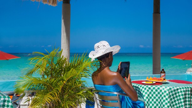 A person sitting at a table with a view of the ocean, under a thatched roof structure.