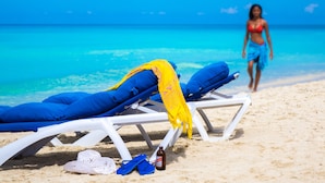 A beach with lounge chairs, a bottle, and flip-flops on the sand.