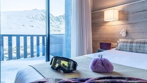 A hotel room with a large window, a bed, a nightstand, and a ski helmet on the bed. - Hotel Caribou (Pas de la Casa)
