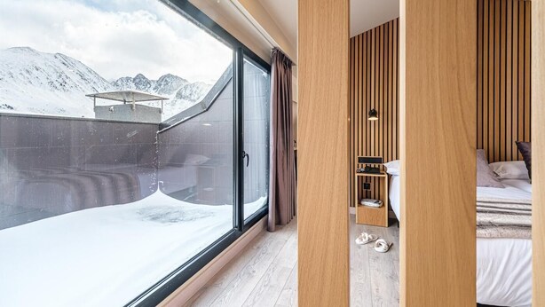 A modern hotel room with a large window offering a view of snow-covered mountains. - Hotel Caribou (Pas de la Casa)