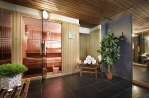 Uma sala de sauna com paredes de madeira, porta de vidro, um banco de madeira e um vaso de planta.