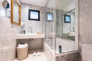 Un baño moderno con paredes de mármol, ducha con cerramiento de vidrio, tocador con espejo y un inodoro.