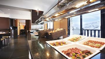Uma área de buffet com diversas opções de comida, um espaço para sentar e vista para as montanhas.