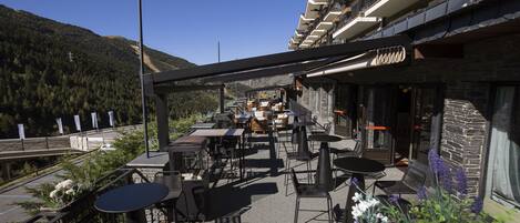 An outdoor patio with tables and chairs, a stone wall, and a view of a mountain.