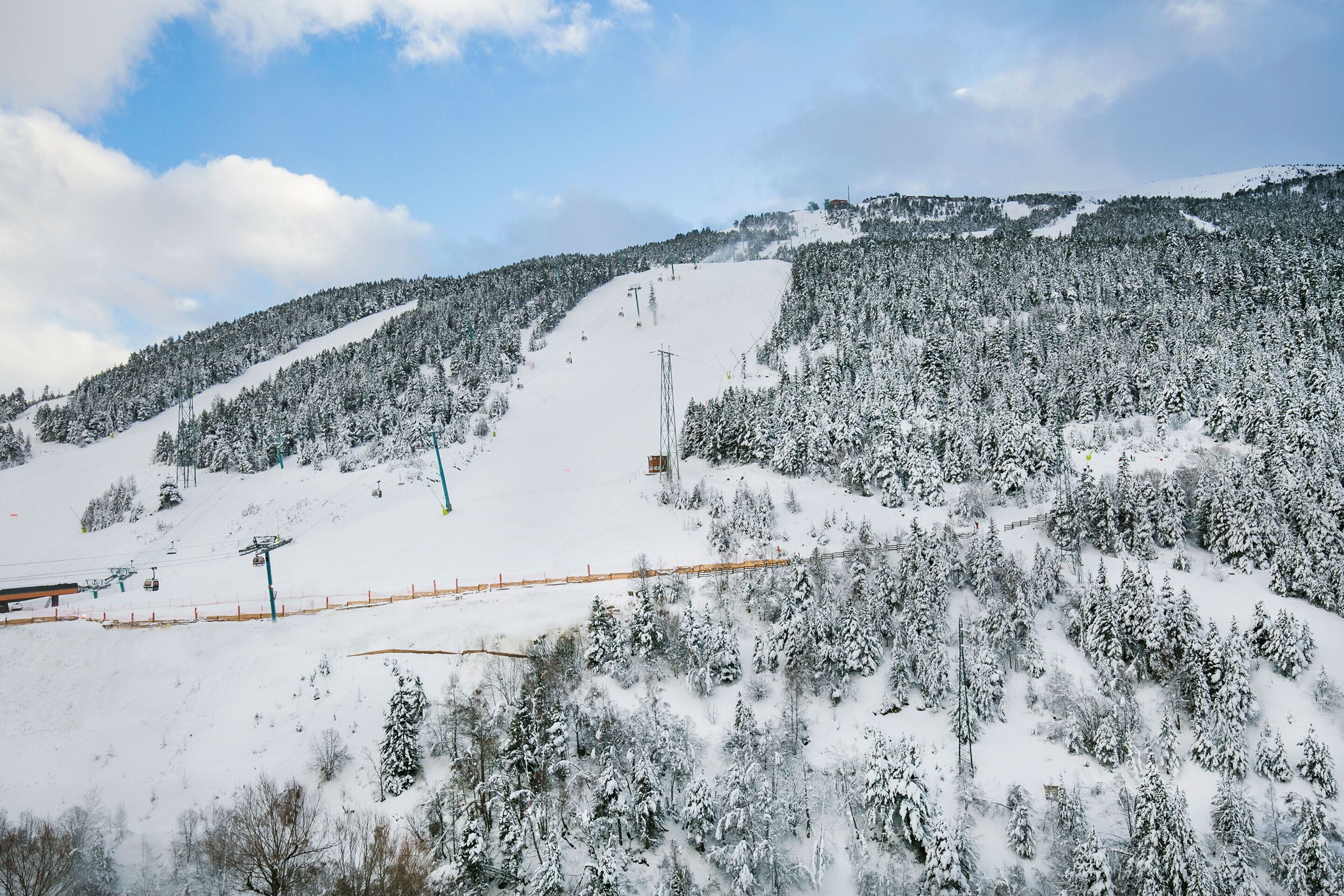 A snow-covered ski slope with ski lifts and a forested mountain.