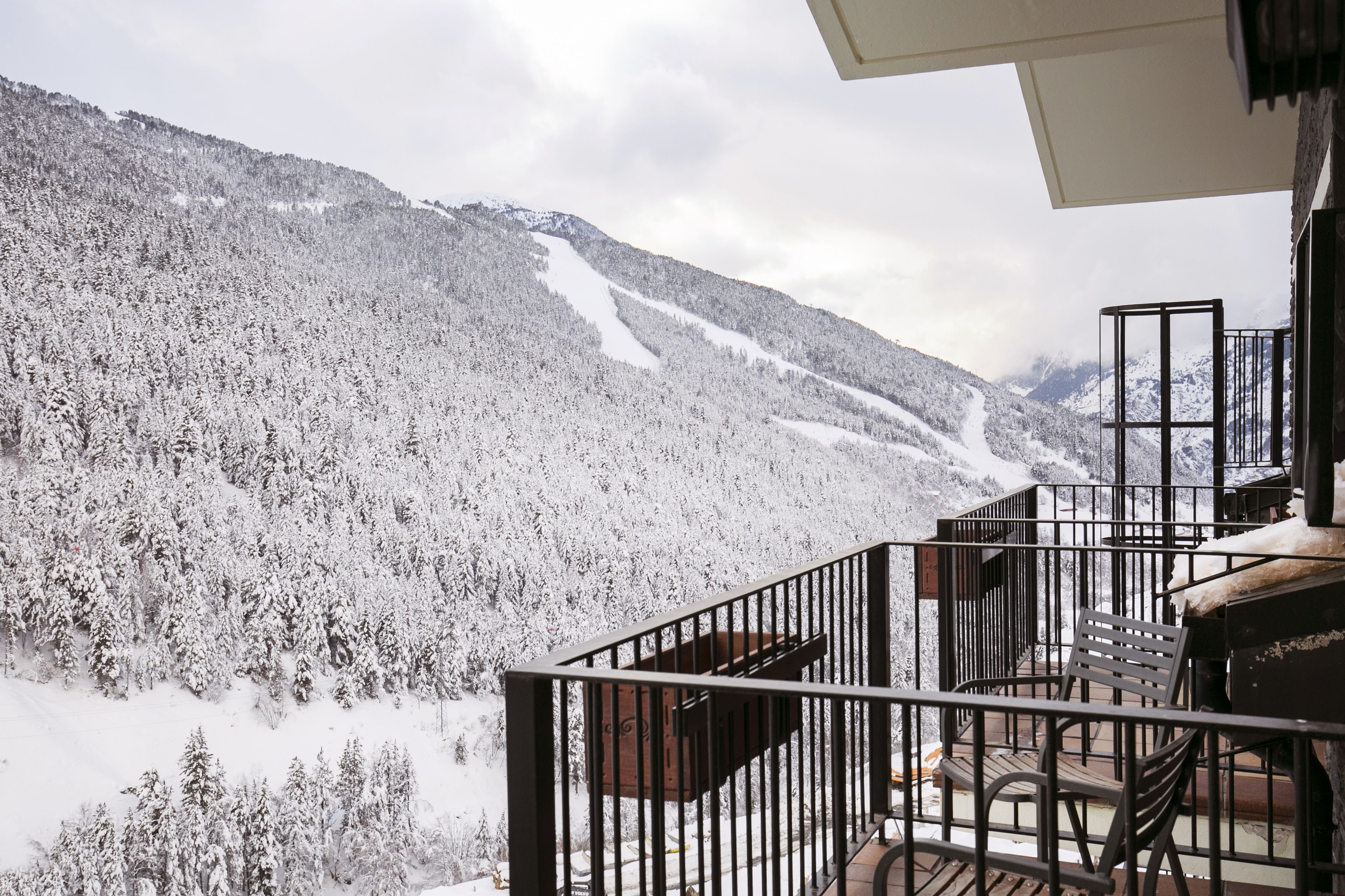 A balcony with a view of a snow-covered mountain and a ski slope.