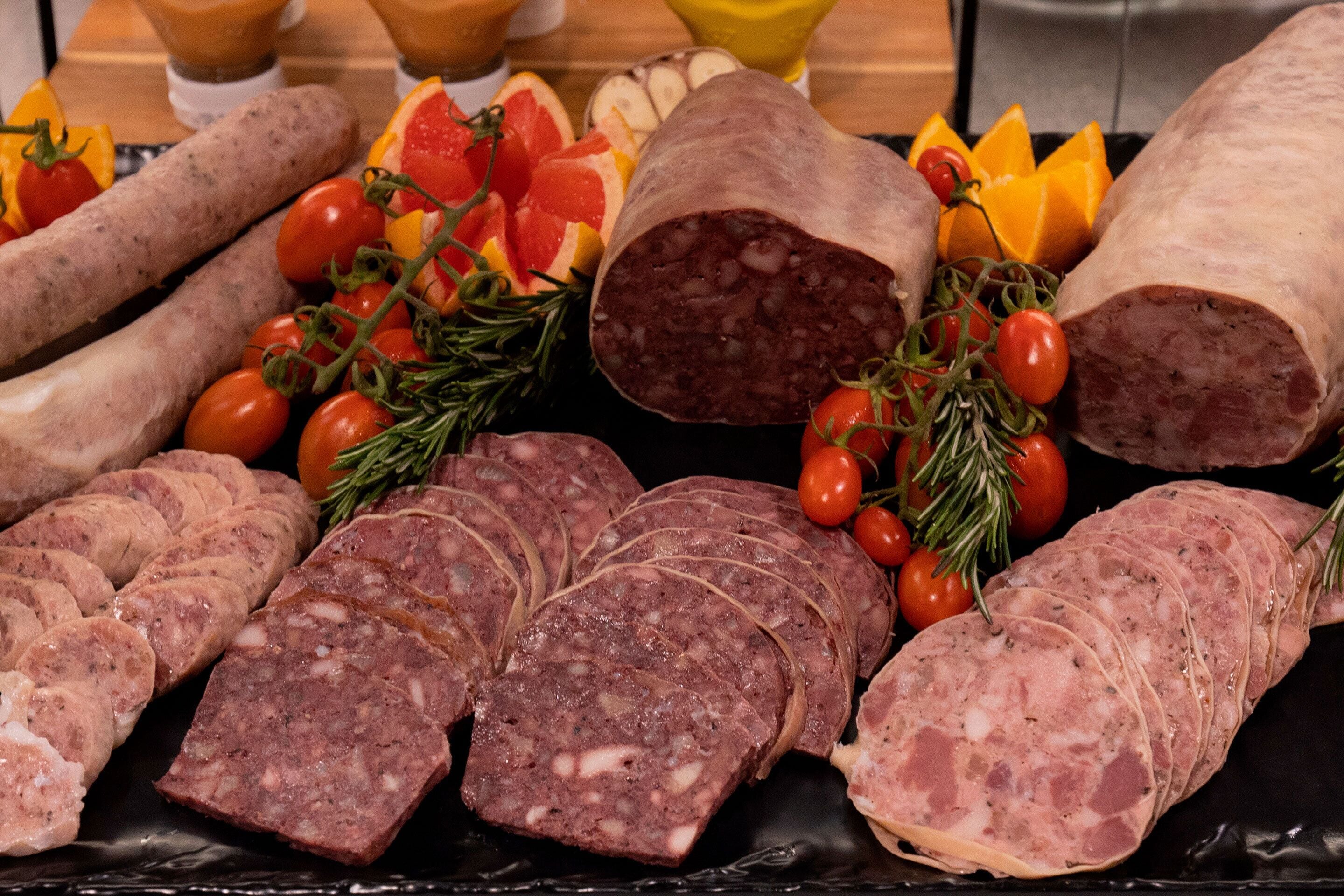 A variety of cured meats and fresh vegetables on a black platter.