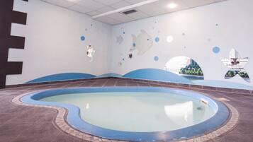 Una piscina con diseño azul y blanco, rodeada de piso y paredes con patrón de olas y decoraciones de peces.