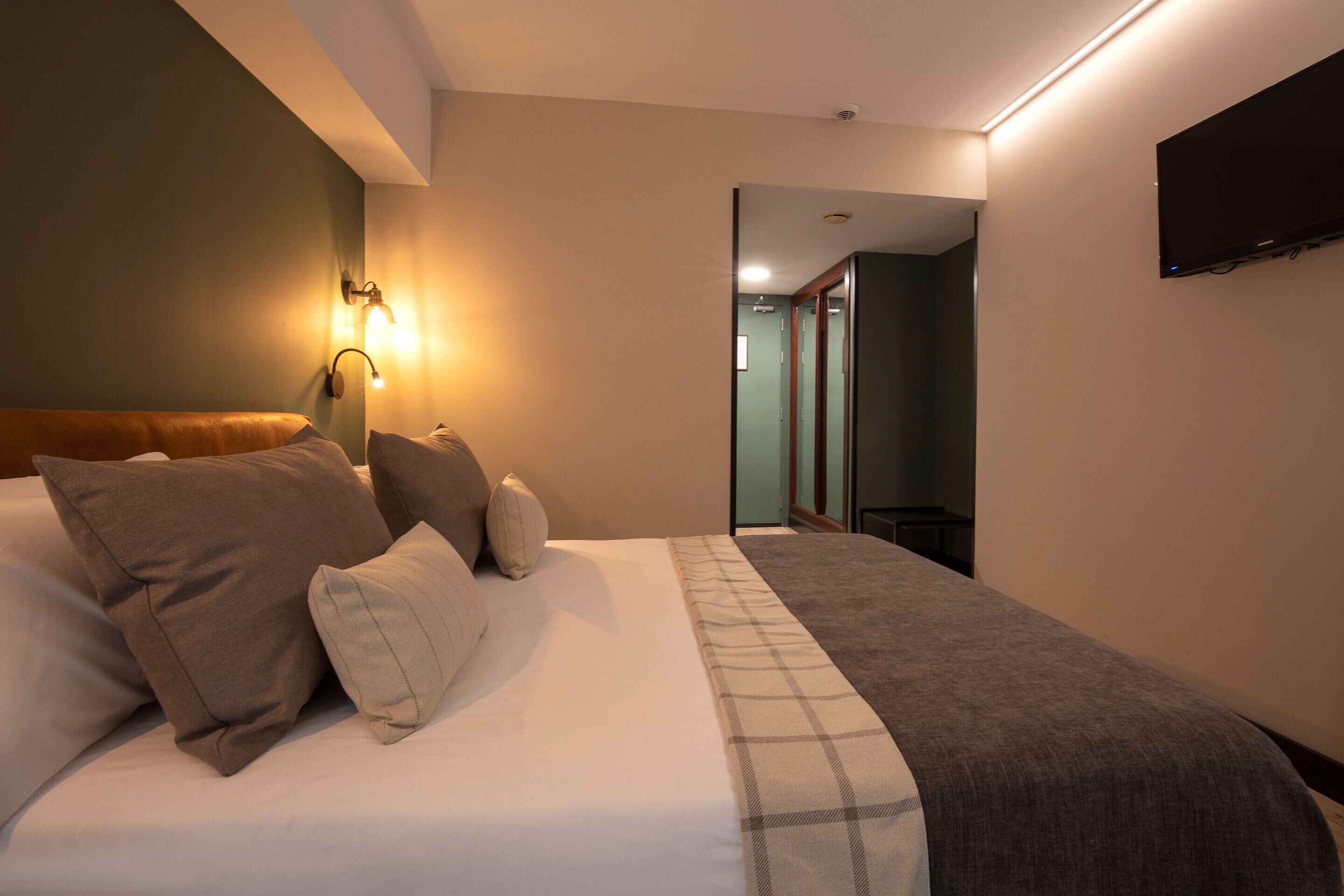 A hotel room with a large bed, a flat-screen TV mounted on the wall, and a hallway leading to another room.