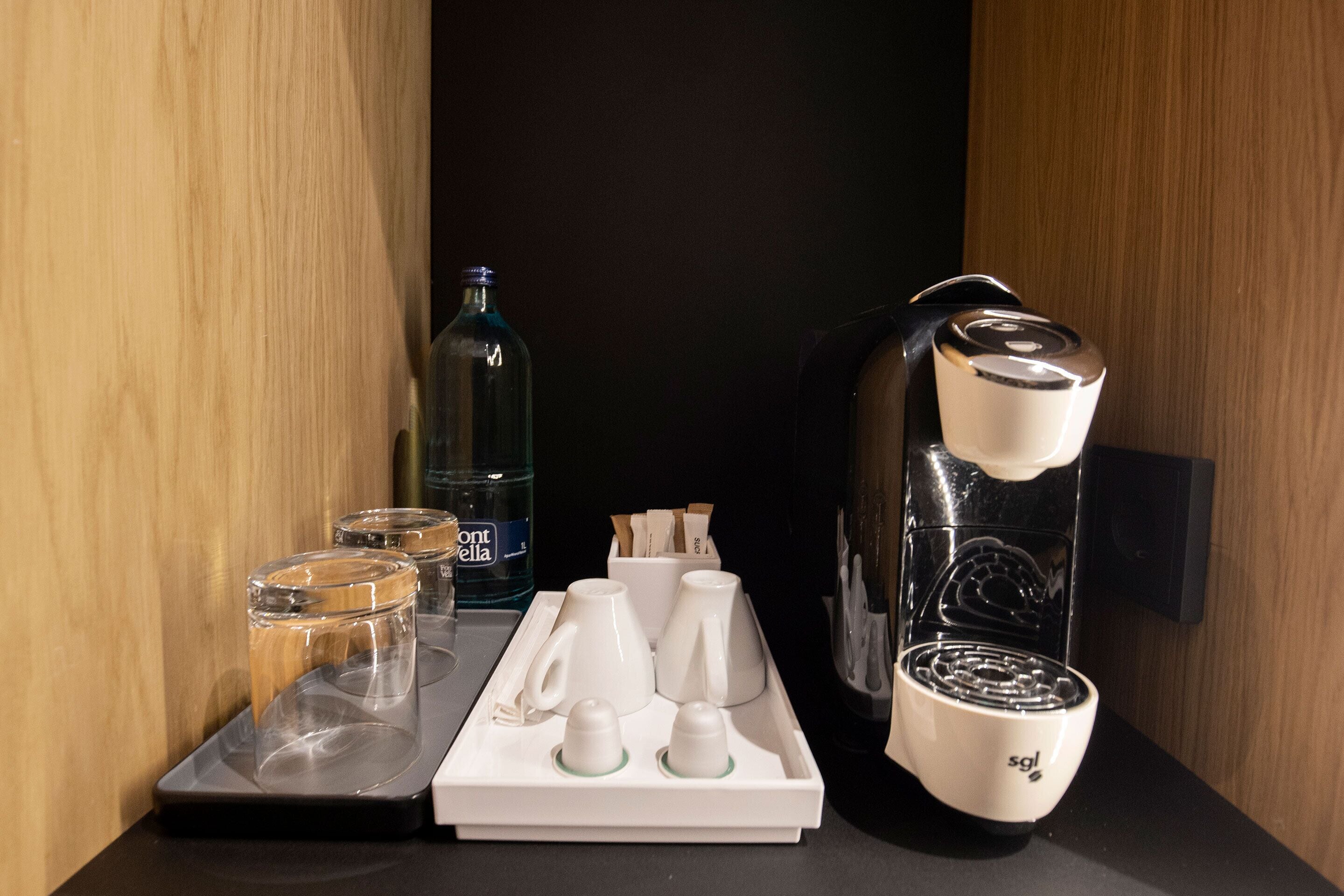 Una estación de café con una máquina de café, tazas y una botella de agua.