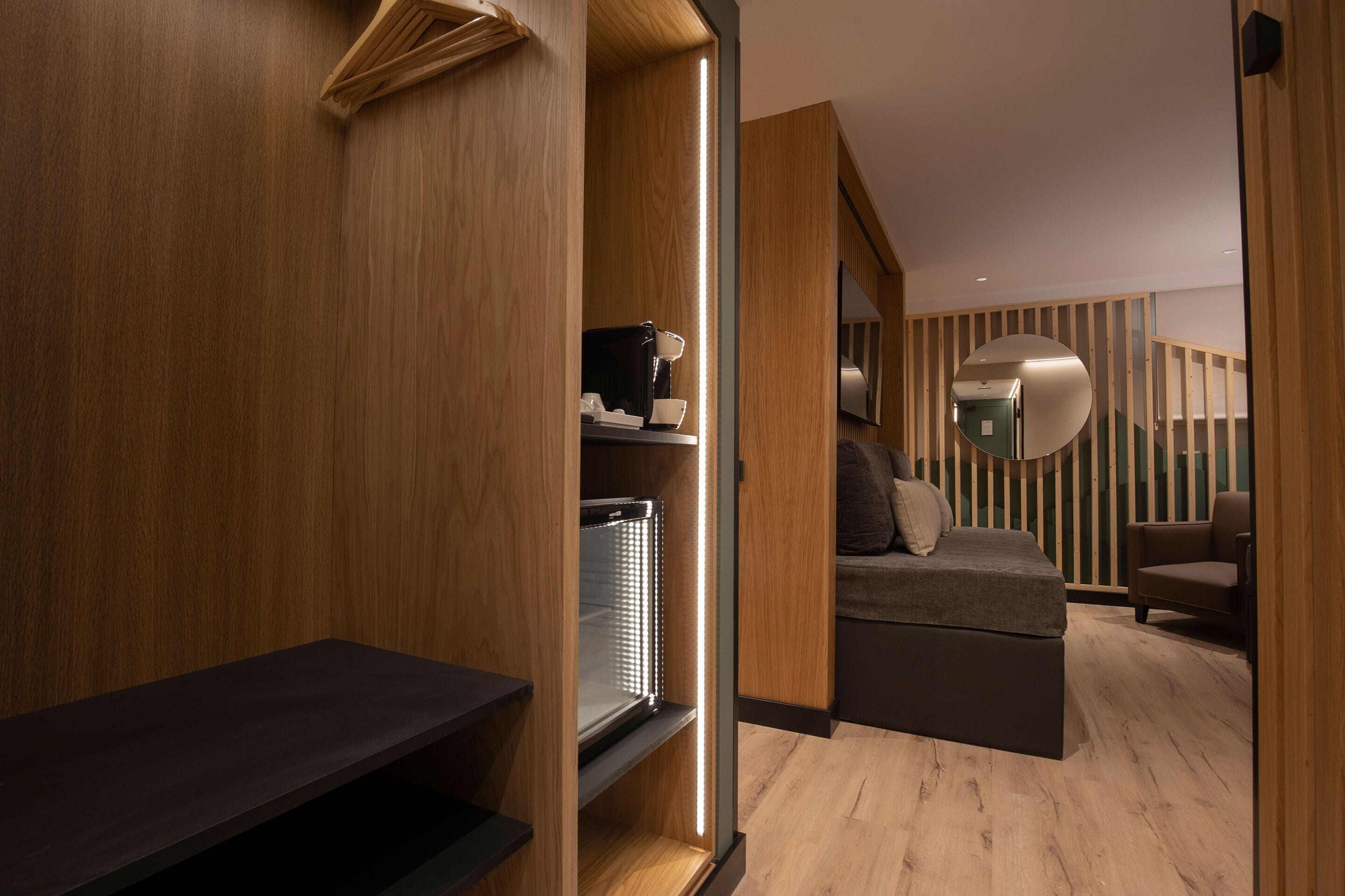 A modern hotel room with a wooden floor, a sofa bed, a coffee machine, and a mirror on the wall.