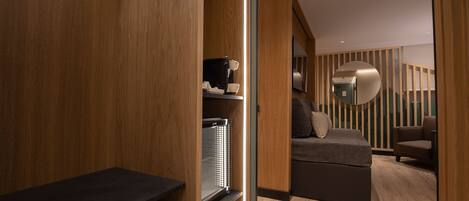 A modern hotel room with a wooden floor, a sofa bed, a coffee machine, and a mirror on the wall.