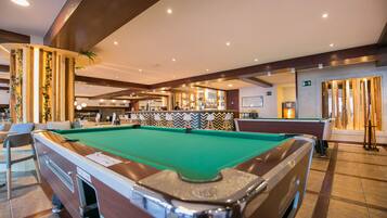 A pool table in a well-lit indoor area with a bar in the background.