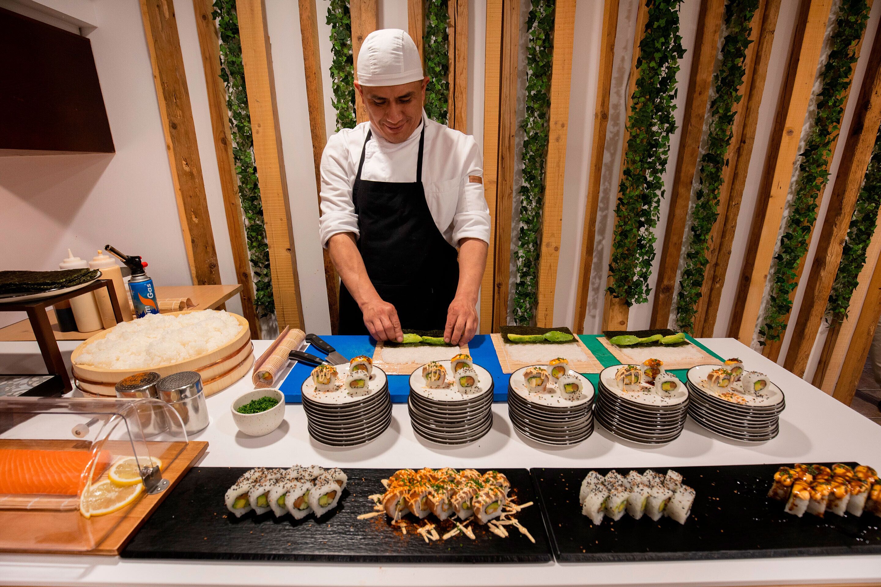 A chef preparing sushi at a counter with various sushi dishes and ingredients.