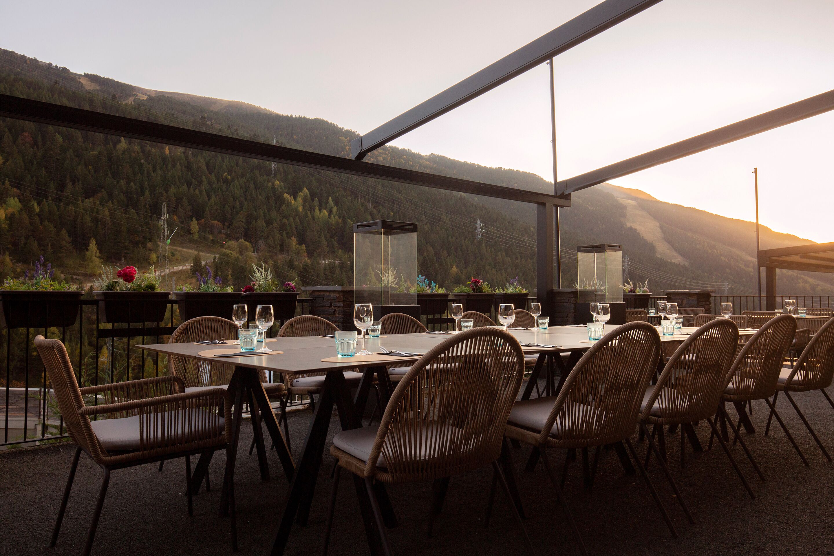 Un espacio de comedor al aire libre con mesas y sillas, con vistas a un paisaje montañoso.
