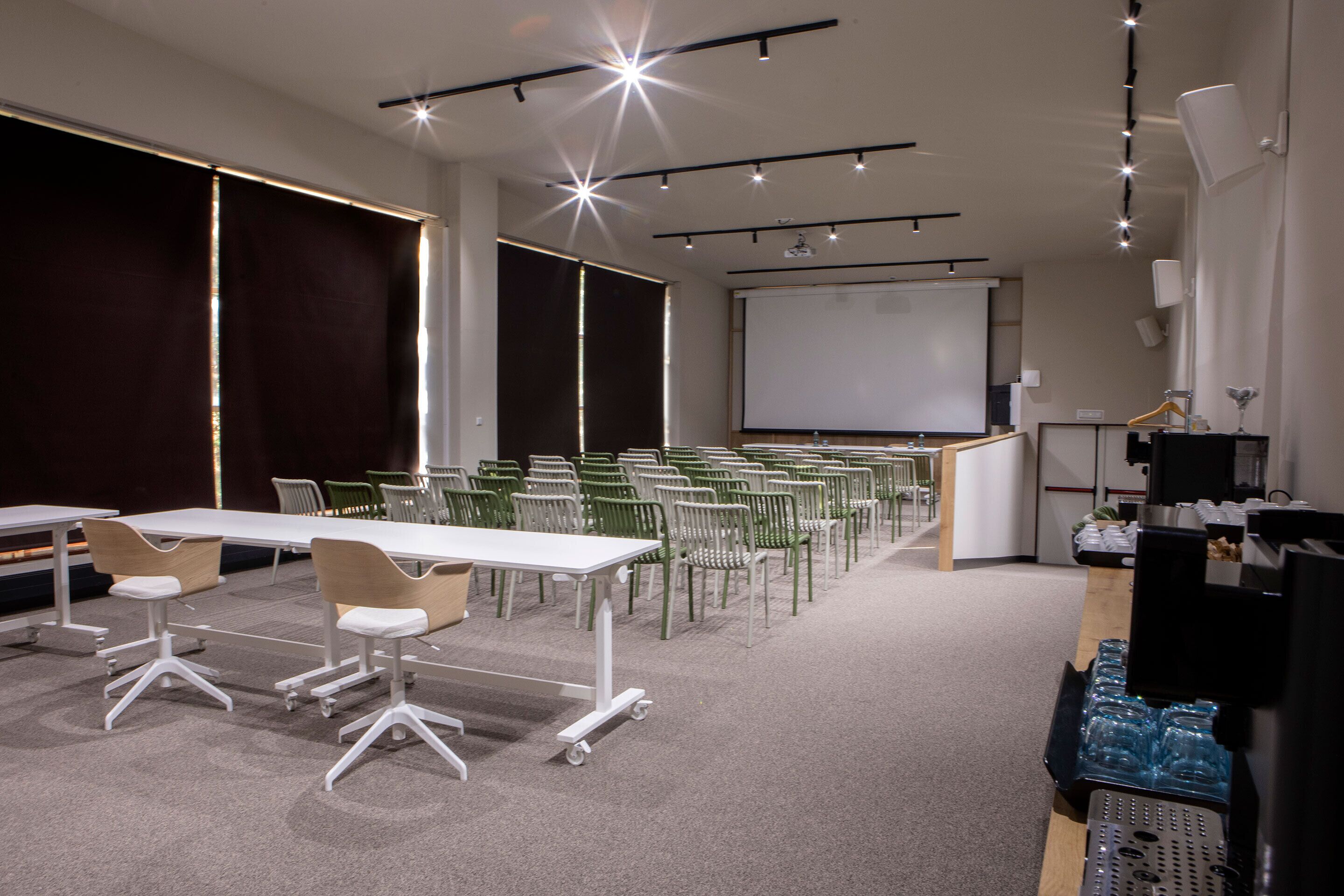 Une salle de conférence avec des rangées de chaises, un tableau blanc et un écran de projection.